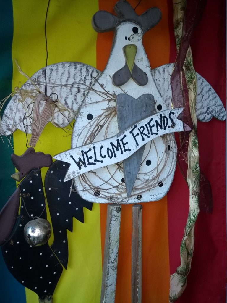 Primitive wooden chicken Welcoming Friends, in front of Pride Flag.